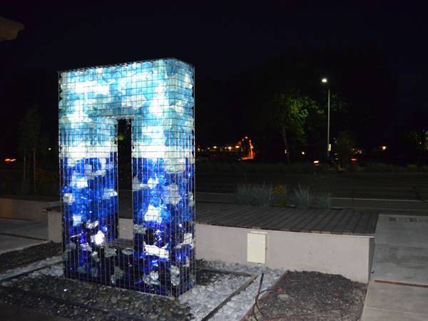 A gabion basket is filled with colored rocks and with LED shining in the dusk.